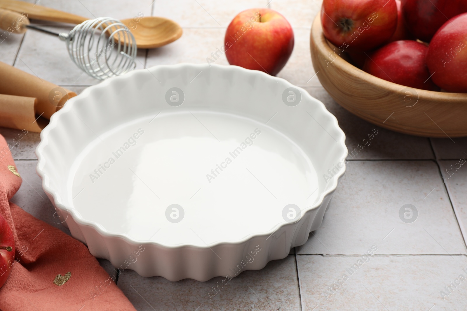 Photo of Ceramic casserole, different cooking utensils and apples on light tiled table, closeup