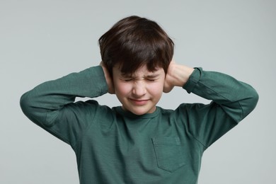 Photo of Annoyed boy covering his ears due to loud sound on grey background