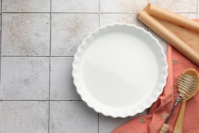 Photo of Ceramic casserole and other cooking utensils on tiled table, flat lay