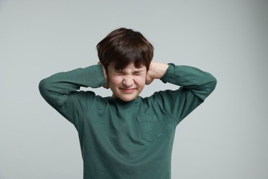 Photo of Annoyed boy covering his ears due to loud sound on grey background