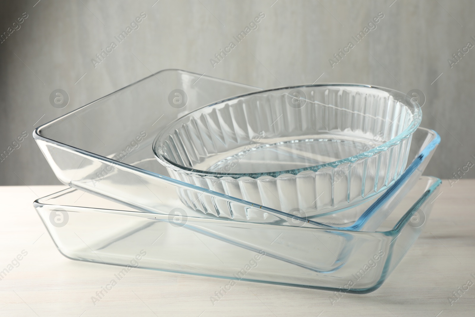 Photo of Different glass casseroles on light wooden table, closeup