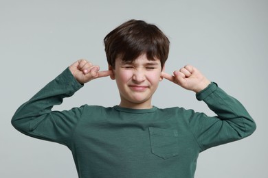 Annoyed boy covering his ears due to loud sound on grey background