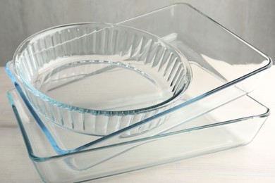 Photo of Different glass casseroles on light wooden table, closeup