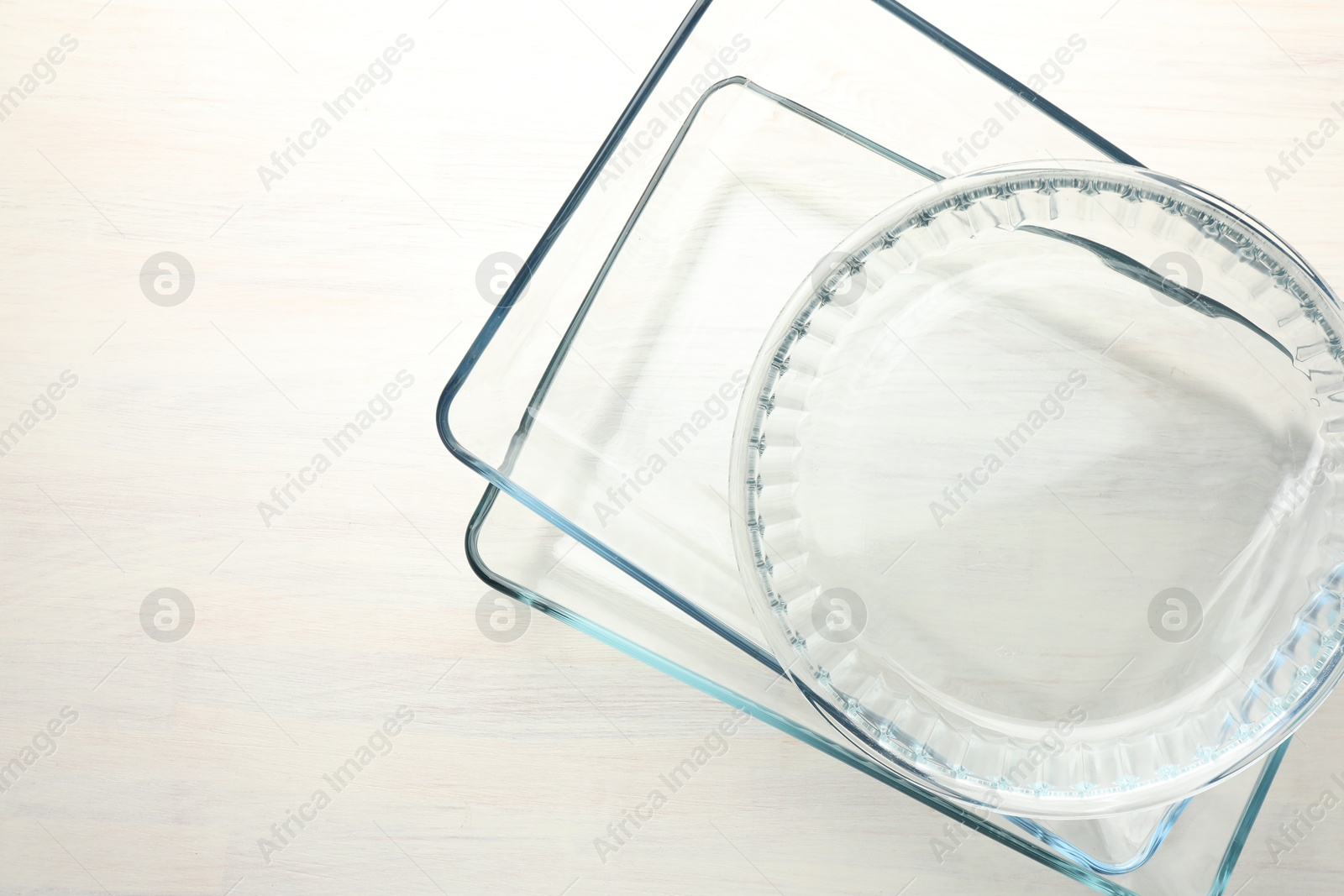 Photo of Different glass casseroles on light wooden table, top view. Space for text