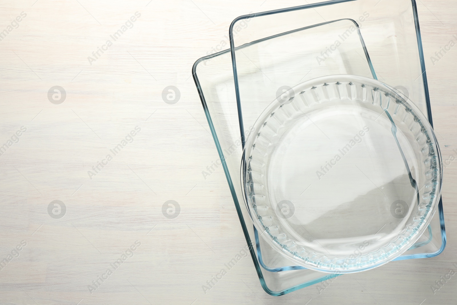 Photo of Different glass casseroles on light wooden table, top view. Space for text