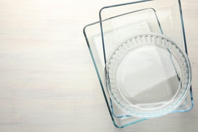 Photo of Different glass casseroles on light wooden table, top view. Space for text