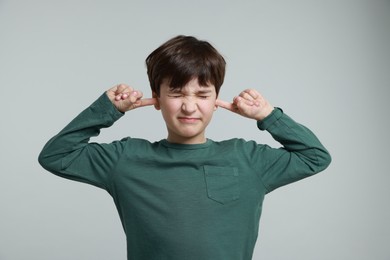 Photo of Annoyed boy covering his ears due to loud sound on grey background