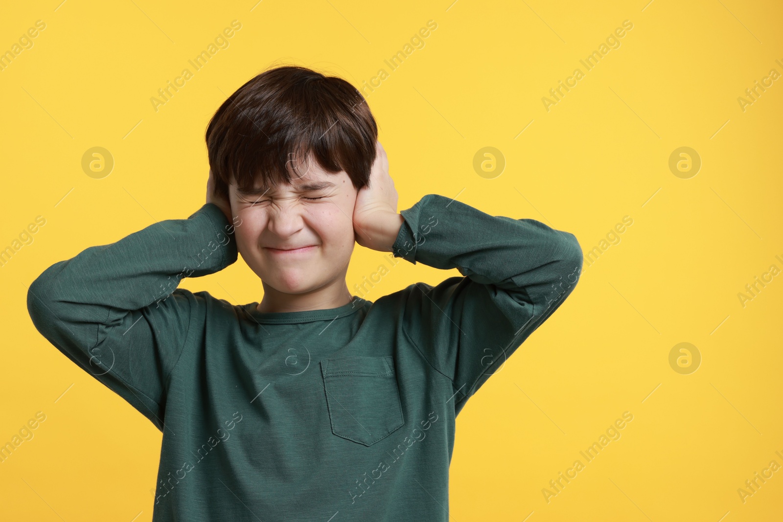 Photo of Annoyed boy covering his ears due to loud sound on yellow background, space for text