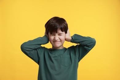 Annoyed boy covering his ears due to loud sound on yellow background