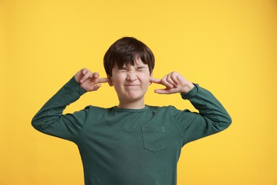 Photo of Annoyed boy covering his ears due to loud sound on yellow background