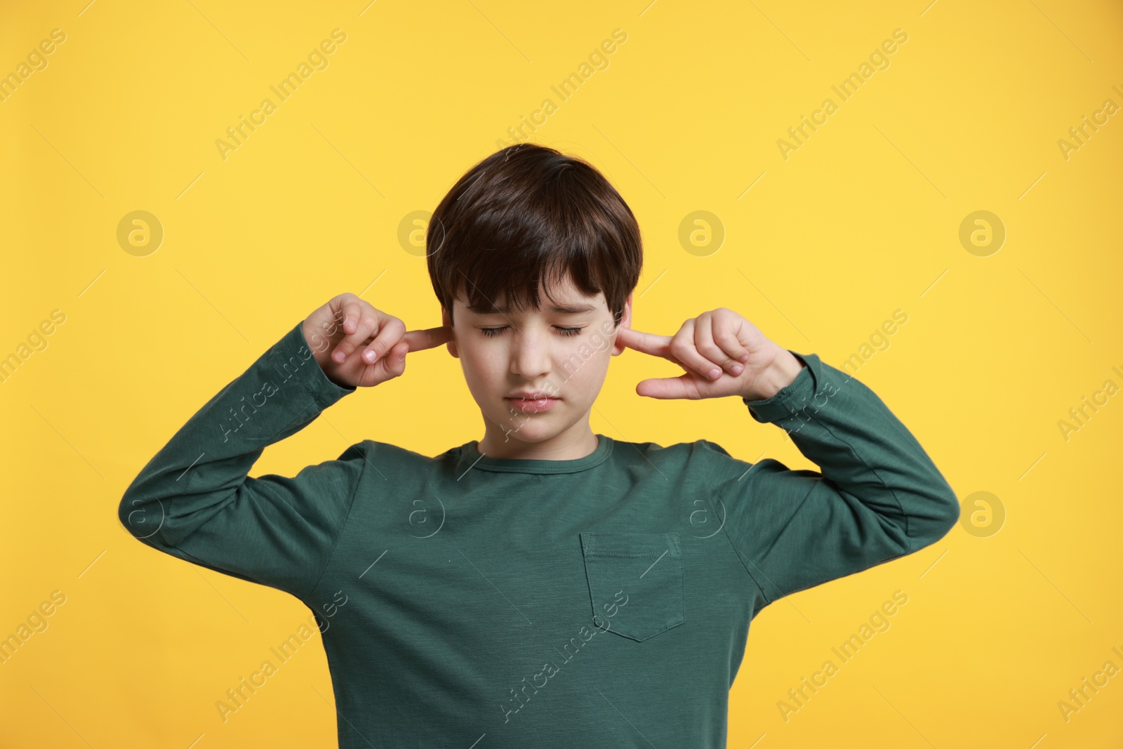 Photo of Annoyed boy covering his ears due to loud sound on yellow background