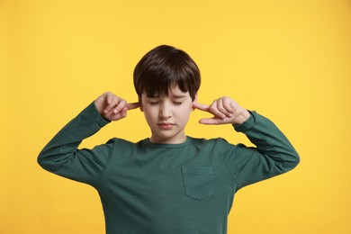 Photo of Annoyed boy covering his ears due to loud sound on yellow background