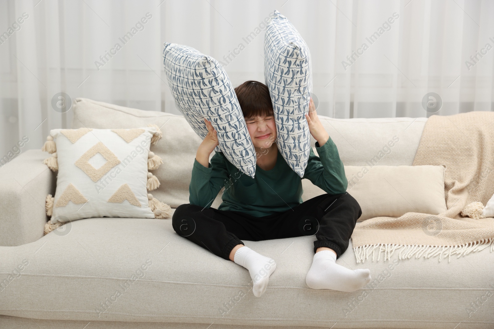 Photo of Annoyed boy covering his ears due to loud sound on sofa at home