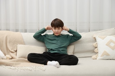 Photo of Annoyed boy covering his ears due to loud sound on sofa at home