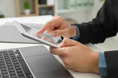 Photo of Businesswoman using tablet at white table indoors, closeup. Modern technology