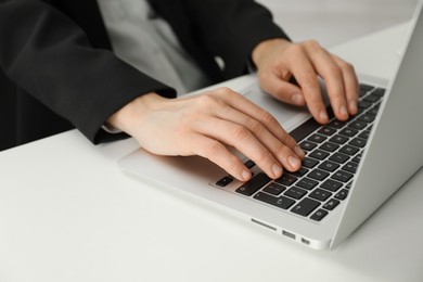 Photo of Businesswoman using laptop at white table indoors, closeup. Modern technology