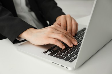 Photo of Businesswoman using laptop at white table indoors, closeup. Modern technology