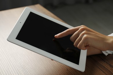 Photo of Businesswoman using tablet at wooden table indoors, closeup. Modern technology