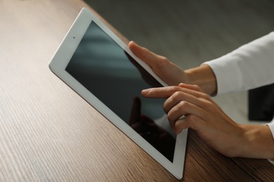 Photo of Businesswoman using tablet at wooden table indoors, closeup. Modern technology