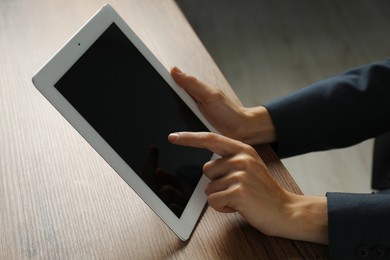 Photo of Businesswoman using tablet at wooden table indoors, closeup. Modern technology