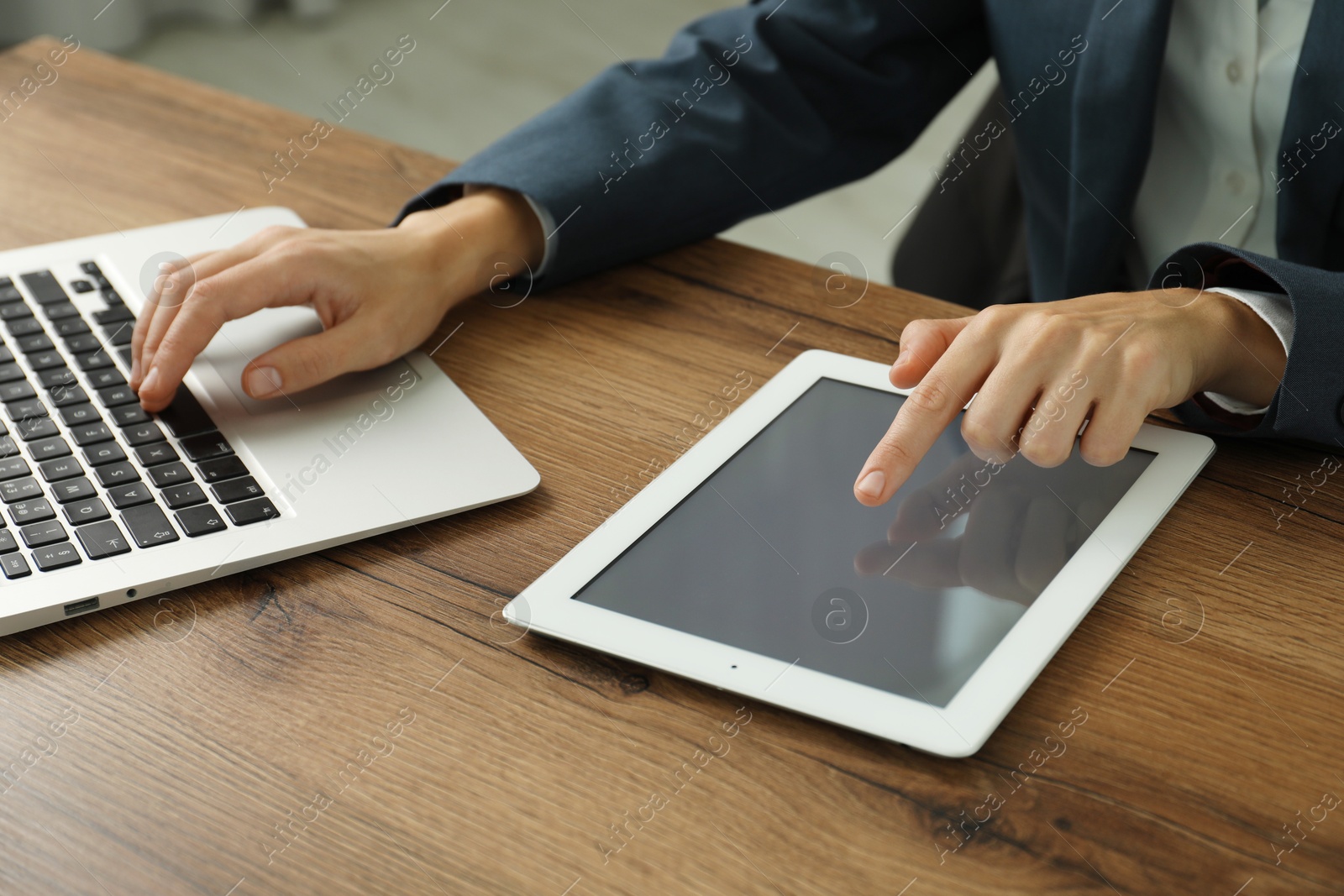 Photo of Businesswoman using laptop and tablet at wooden table indoors, closeup. Modern technology