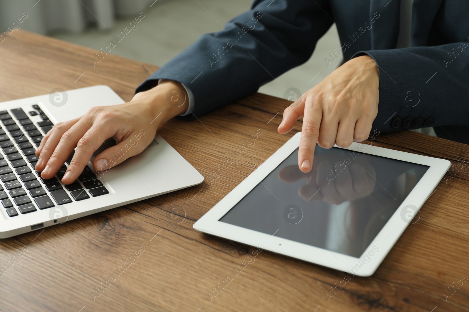 Photo of Businesswoman using laptop and tablet at wooden table indoors, closeup. Modern technology