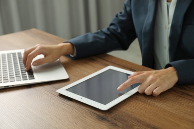 Photo of Businesswoman using laptop and tablet at wooden table indoors, closeup. Modern technology