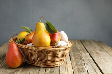 Photo of Ripe juicy pears in wicker basket on wooden table against grey background