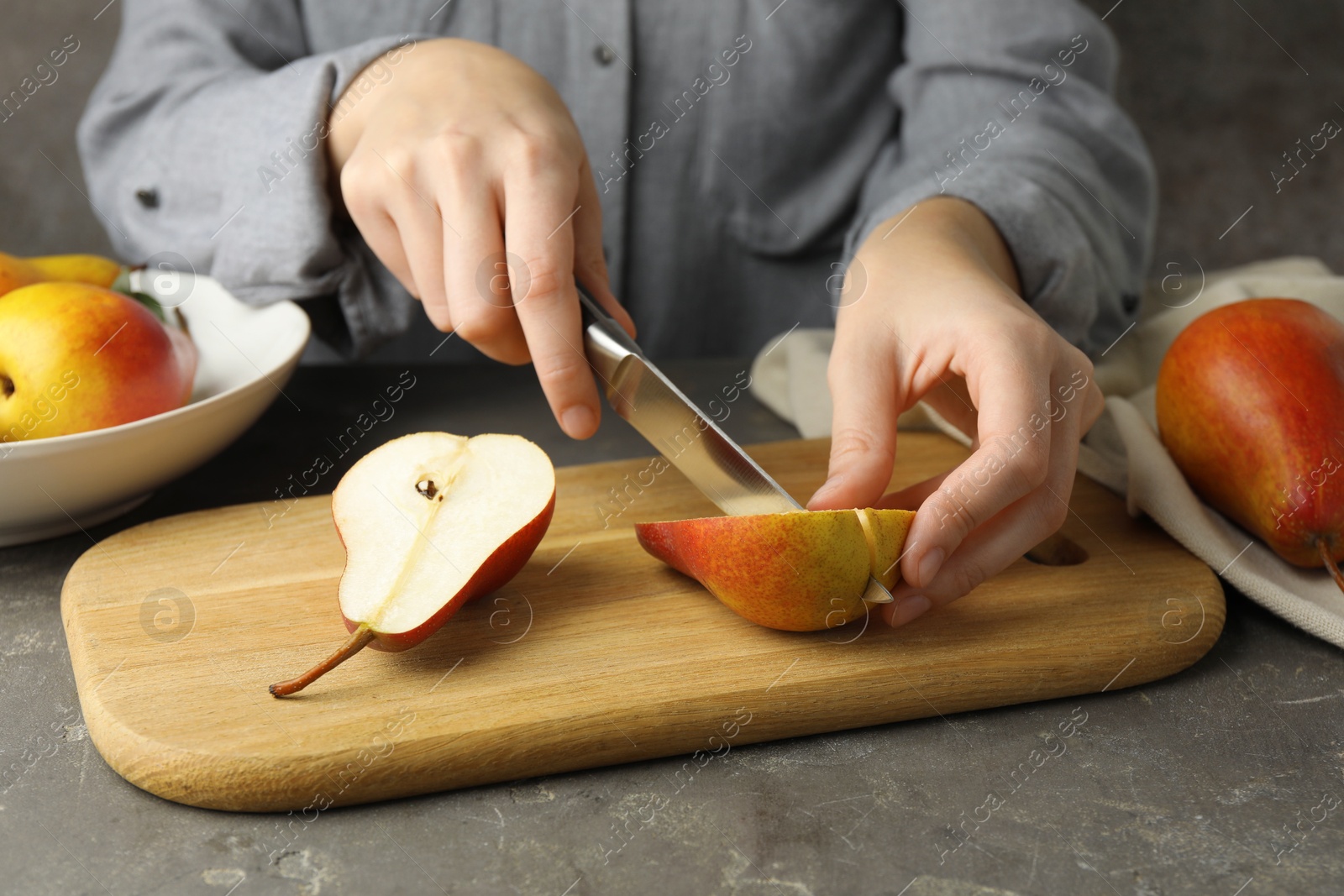 Photo of Woman cutting pear at grey textured table, closeup