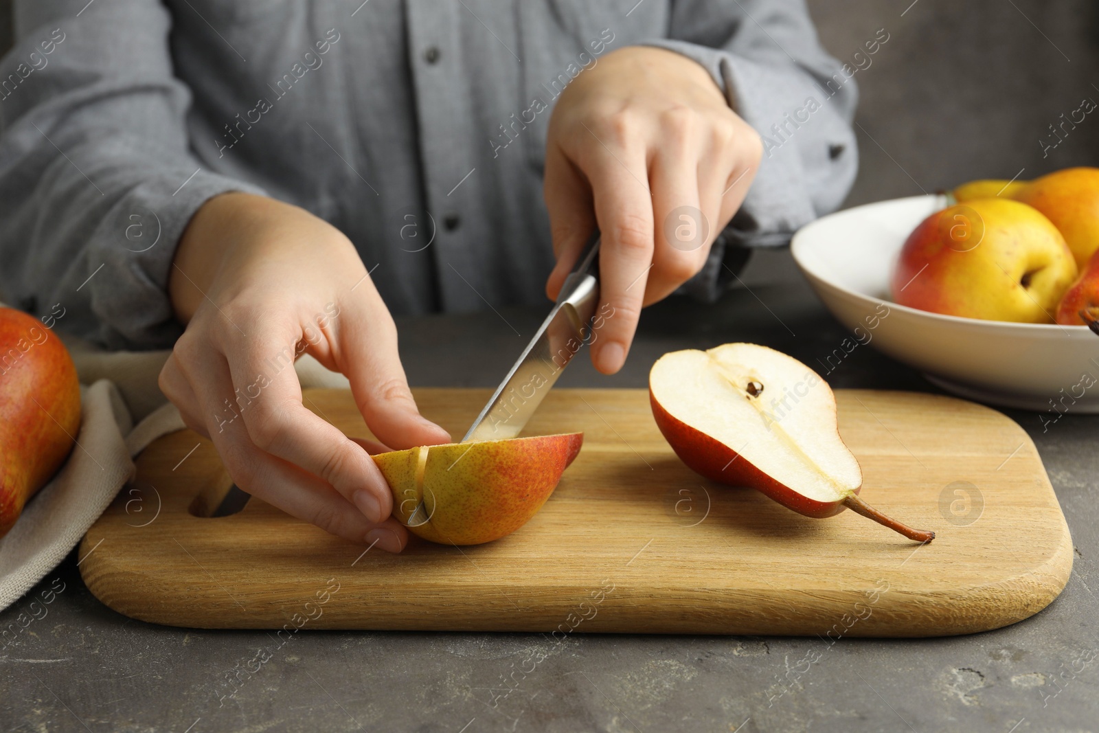 Photo of Woman cutting pear at grey textured table, closeup