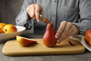 Photo of Woman cutting pear at grey textured table, closeup