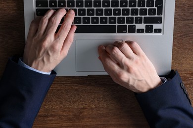 Photo of Businessman using laptop at wooden table, top view. Modern technology