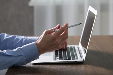 Photo of Businessman using laptop at wooden table indoors, closeup. Modern technology