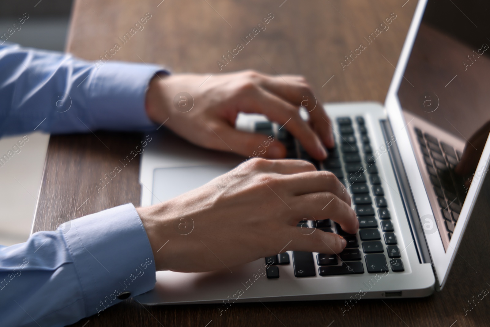 Photo of Businessman using laptop at wooden table indoors, closeup. Modern technology