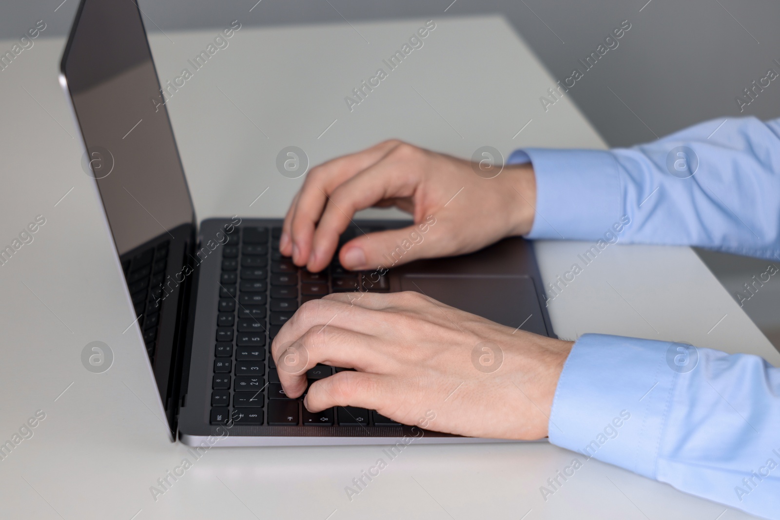 Photo of Businessman using laptop at white table indoors, closeup. Modern technology