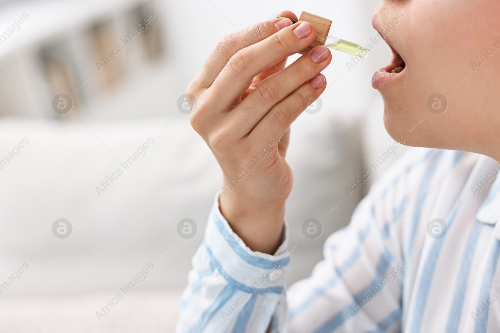 Photo of Young woman taking CBD tincture indoors, closeup. Space for text