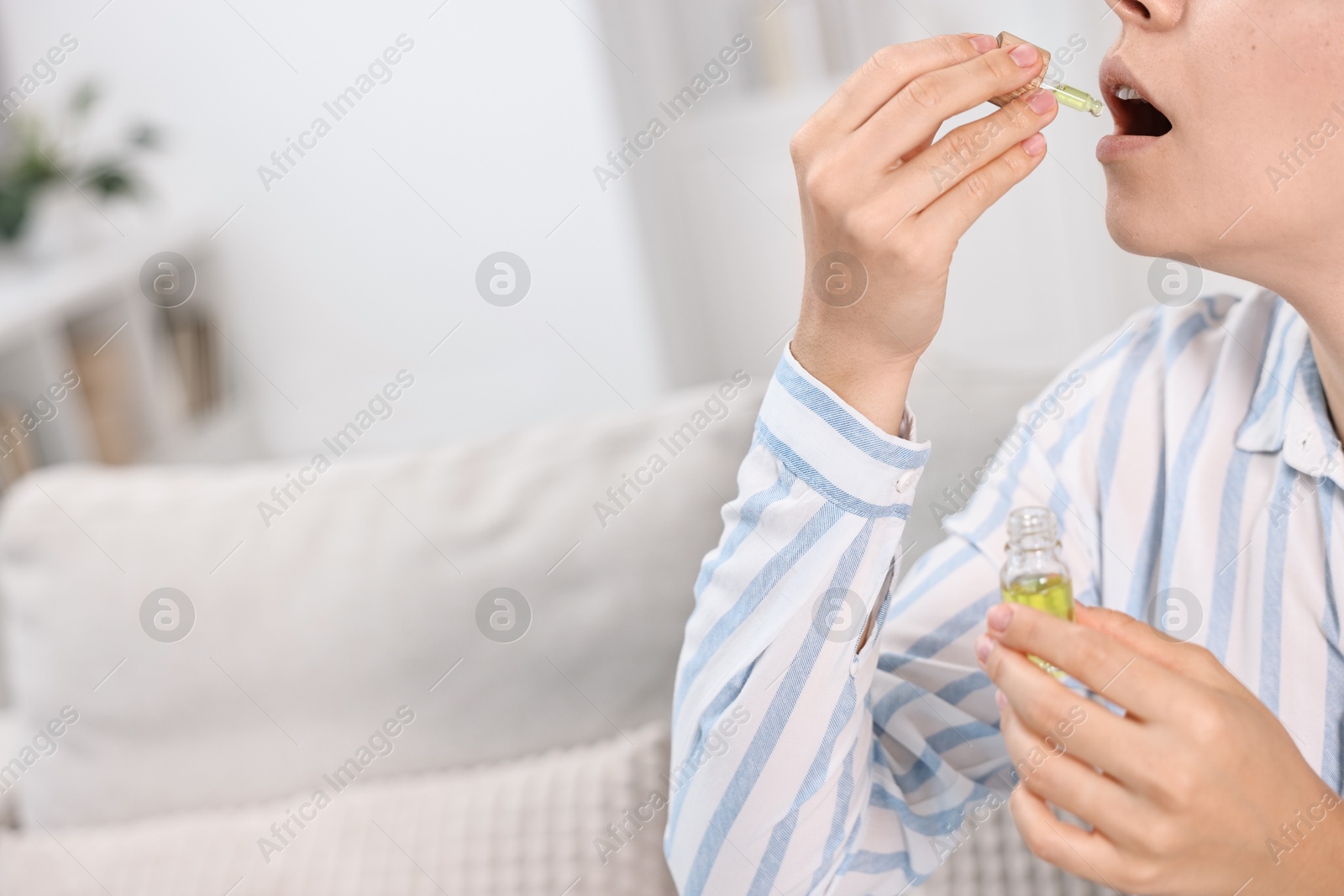 Photo of Young woman taking CBD tincture indoors, closeup. Space for text