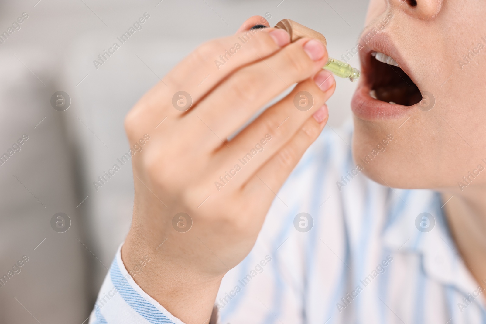 Photo of Young woman taking CBD tincture indoors, closeup