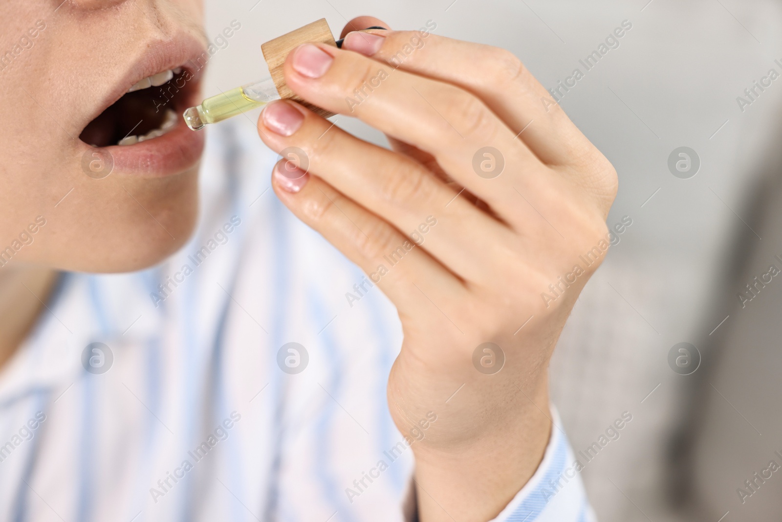 Photo of Young woman taking CBD tincture indoors, closeup