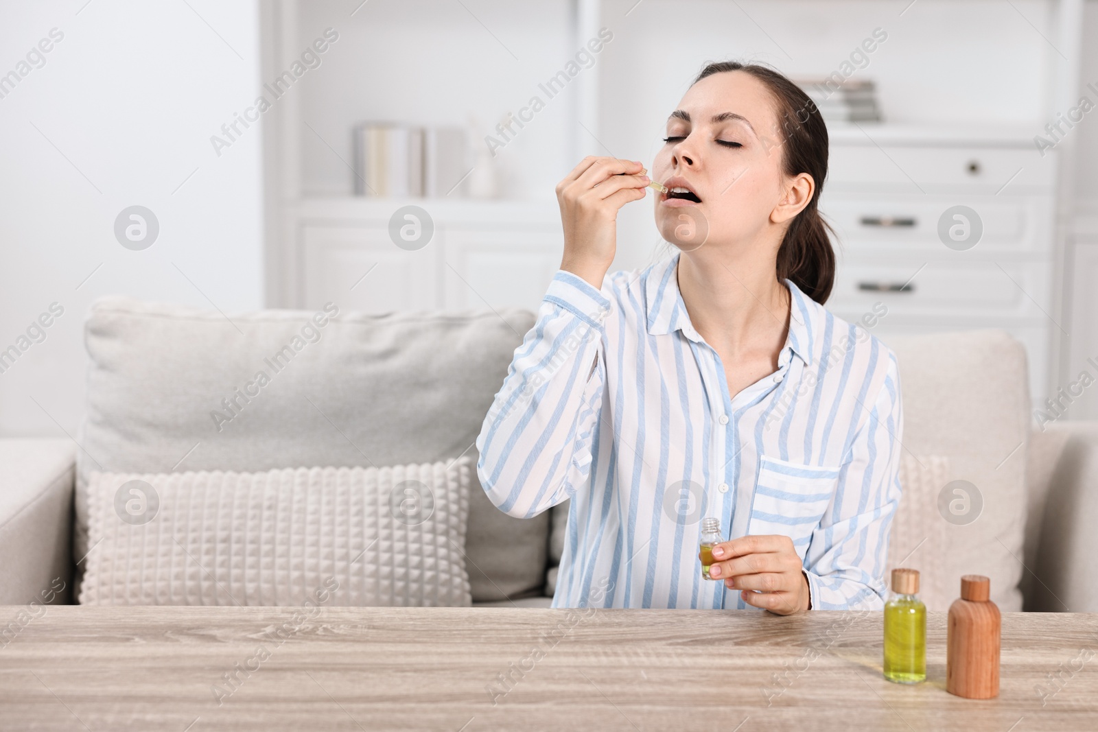 Photo of Young woman taking CBD tincture at wooden table indoors, space for text