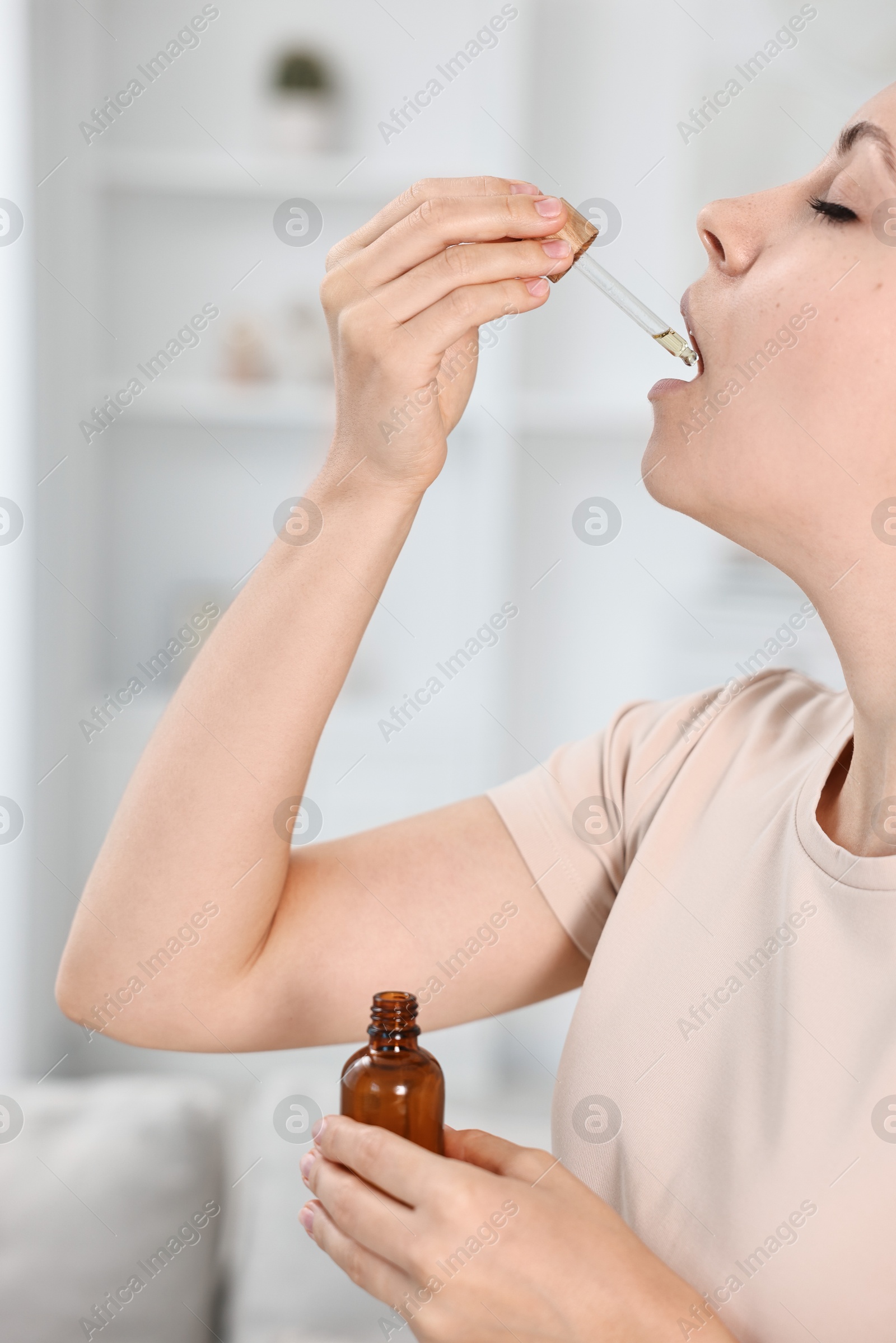 Photo of Young woman taking CBD tincture indoors. Herbal extract