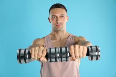 Man exercising with dumbbells on light blue background