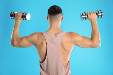 Photo of Man exercising with dumbbells on light blue background, back view