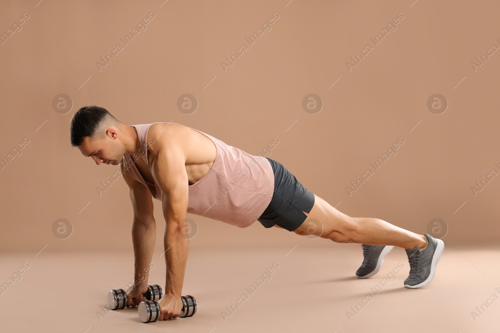 Photo of Man exercising with dumbbells on light brown background