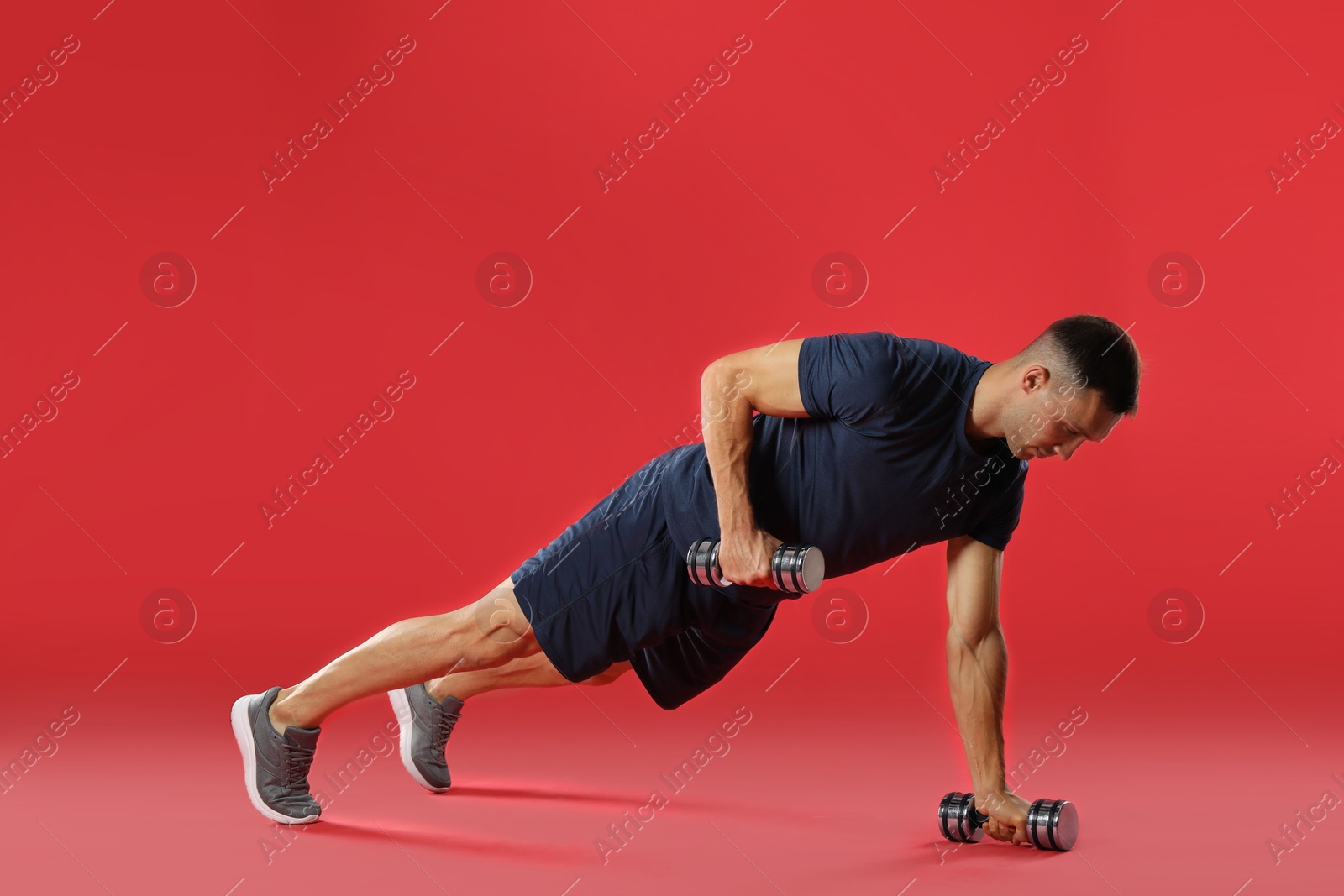 Photo of Man exercising with dumbbells on red background