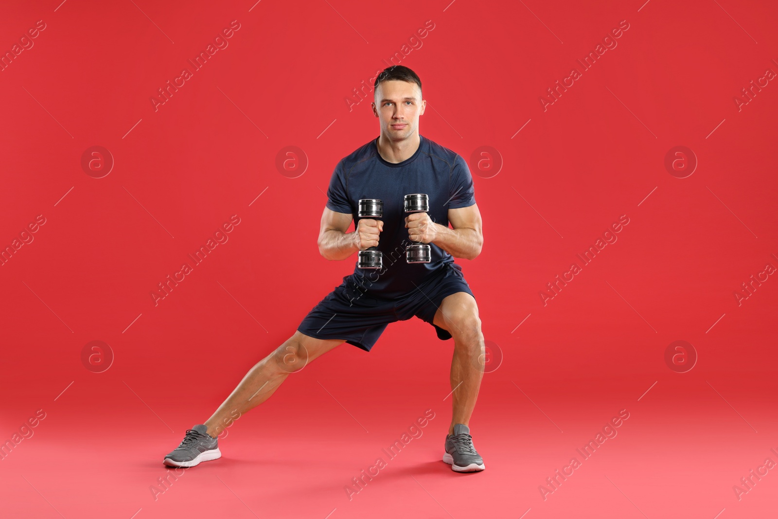 Photo of Man exercising with dumbbells on red background