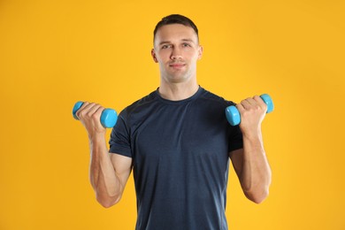 Man exercising with dumbbells on yellow background