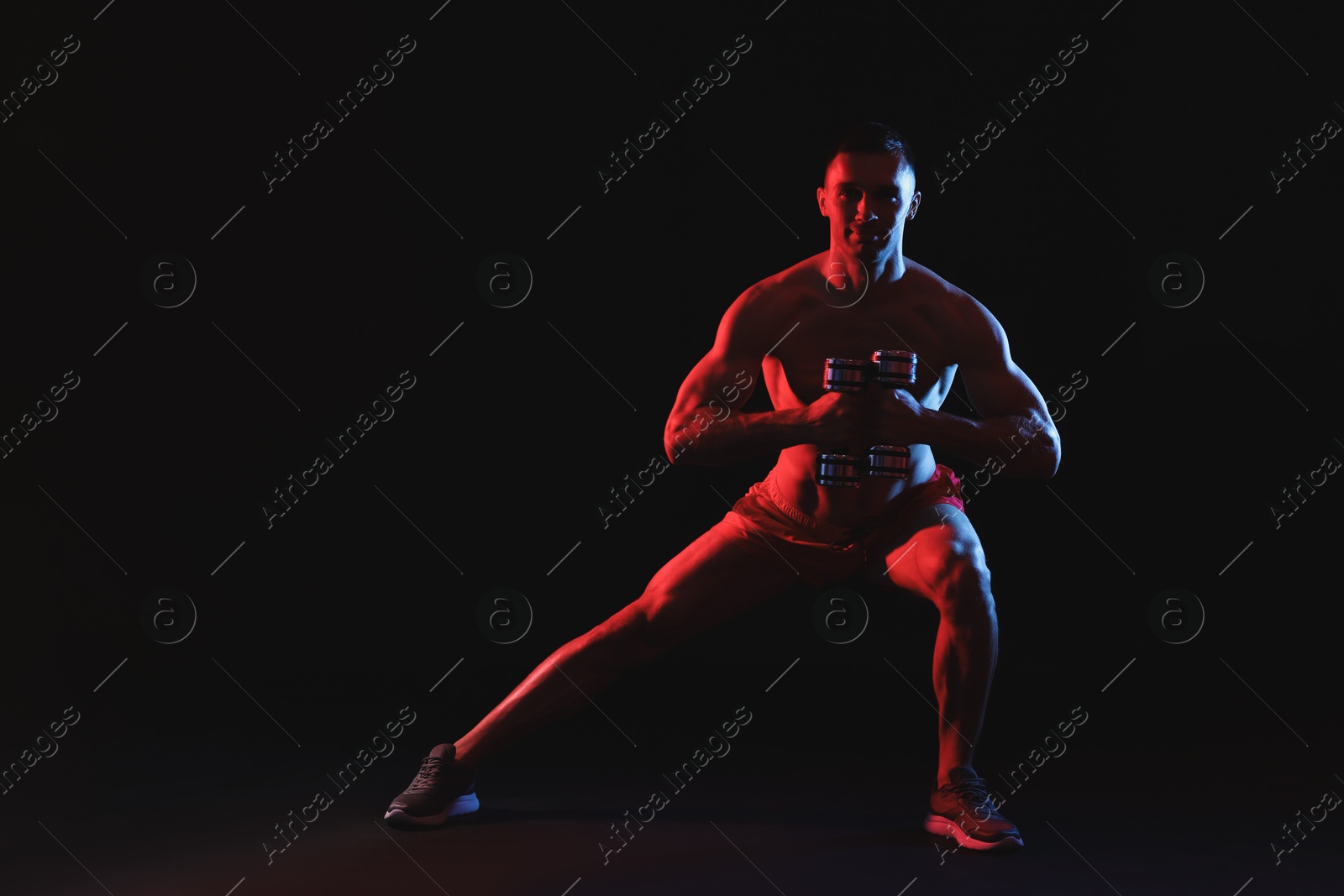 Photo of Man exercising with dumbbells in red light on black background