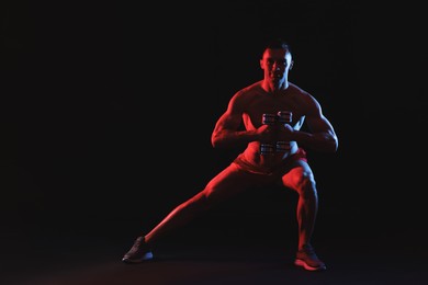 Photo of Man exercising with dumbbells in red light on black background