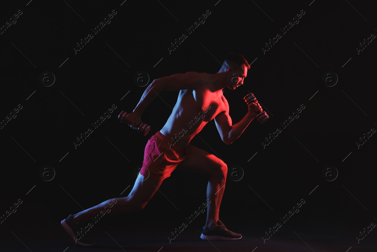 Photo of Man exercising with dumbbells in red light on black background